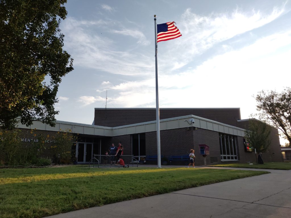 elementary school with American flag  and children playing in front of it
