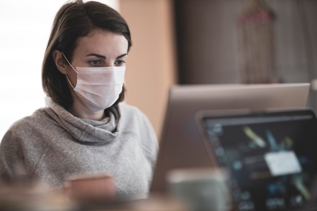 Woman sitting at computer with surgical mask on.
